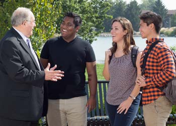 A professor and 3 students talk outside by a lake