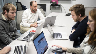Students with laptops studying at a table.