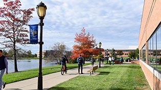 Campus view students on sidewalk, sunny day with blue sky.