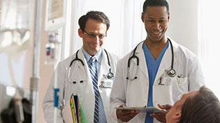 Two doctors in white lab coats speaking with a patient.