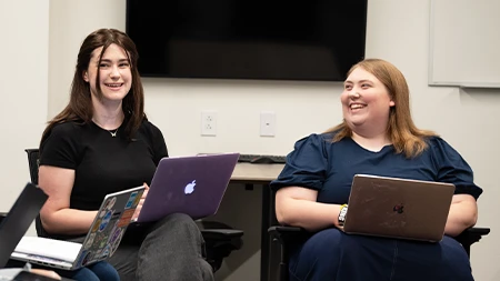 Two students with laptops talking and laughing.