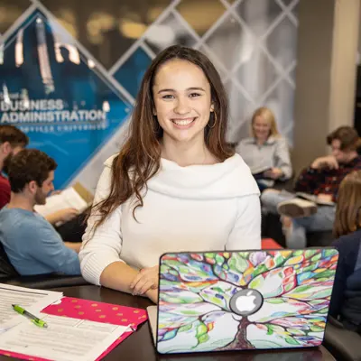 Female student studying at a table with a laptop and notebook.