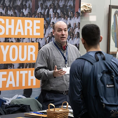 Missions conference, missionary table host speaking with student.