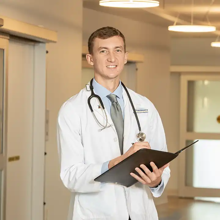 Male phamacy student wearing a stethoscope taking notes.