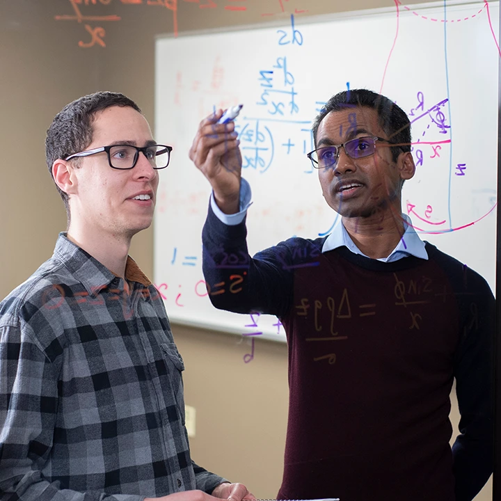 Two male students performing math equations on a glass wall.