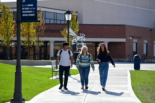 Three Cedarville University students walk together on a sunny campus sidewalk near the student center.