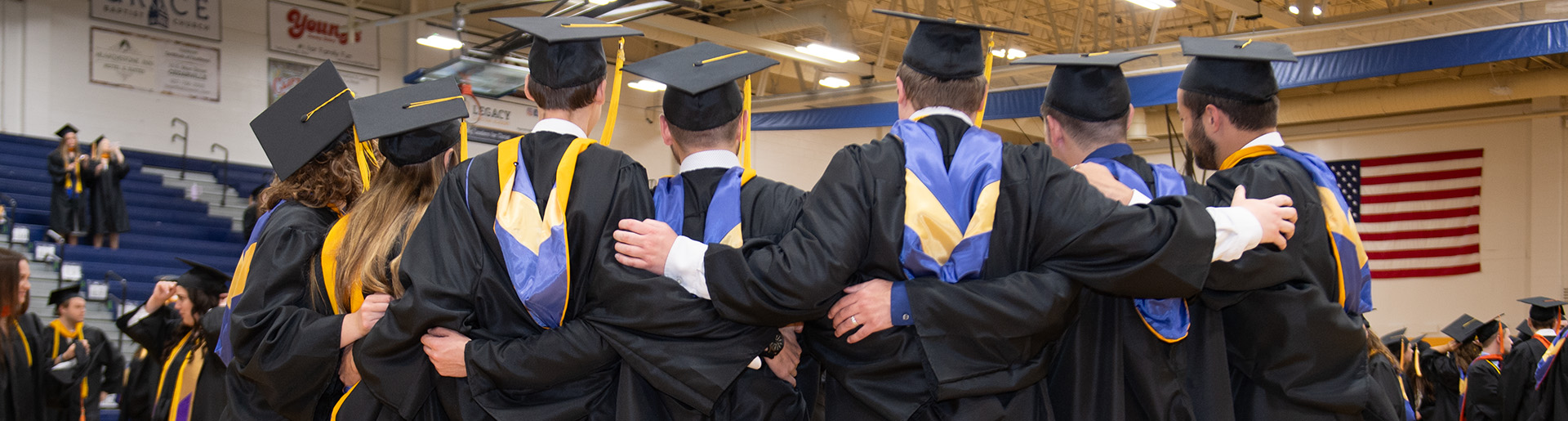 Cedarville University graduates in caps and gowns with arms around each other.