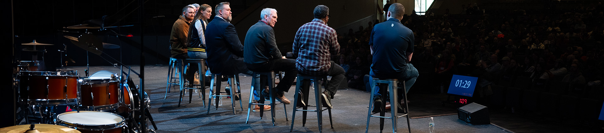 Seven men and women seated on stools lead a discussion about worship on the Cedarville chapel stage.