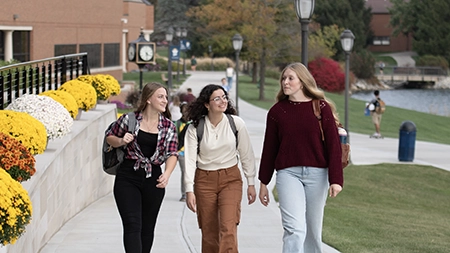 three female students walking outdoors on campus in the fall semester