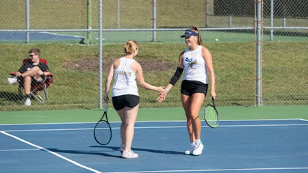 Two girls high five on tennis court