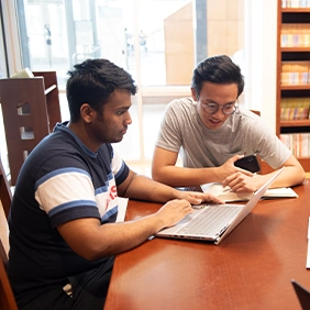 Two male college students sitting at a desk looking at a laptop