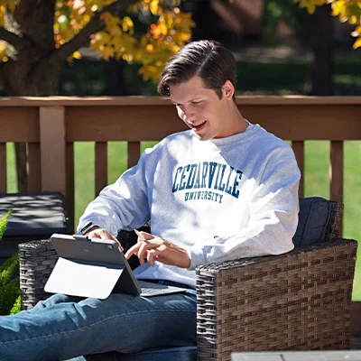 Student sitting outside on porch studying on tablet.