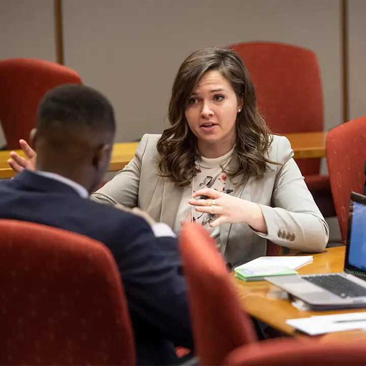 Man and woman in business attire sitting and talking at a conference table.
